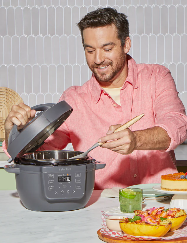 A man in a coral shirt smiles while stirring food inside the Instant Pot® RIO™ Mini 4QT Multi-Cooker in Truffle.